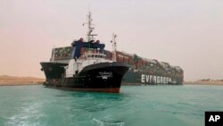 Un barco navega frente al enorme carguero que tras perder energía encalló y se cruzó de lado a lado en el Canal de Suez, bloqueando la importante vía de transporte marítimo mundial.