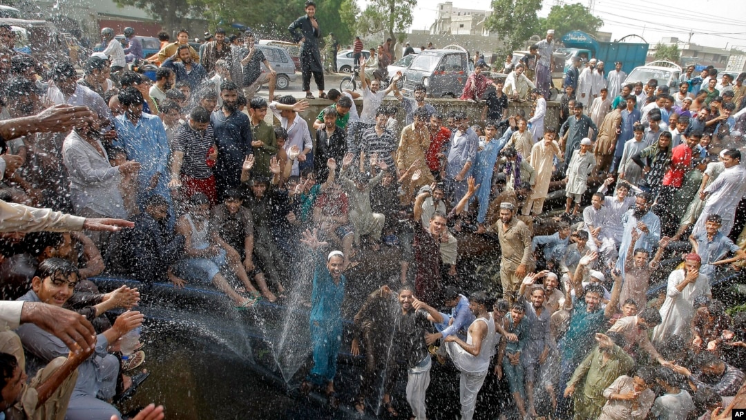 FILE - People cool off in a spray from a broken water pipe during a heat wave, in Karachi, Pakistan, May 31, 2017. 