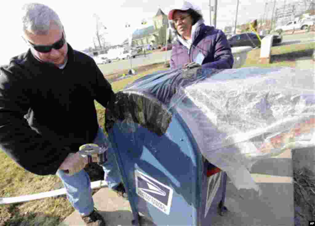 Indiana post office regional manager Doug Caswell, left, and Lisa Smith wrap a post box after it was destroyed by a tornado in Henryville, Ind., Sunday, March 4, 2012.