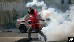 A Thai anti-government protester throws back tear gas canister at riot policemen during a clash at a sport stadium in Bangkok, Dec. 26, 2013.