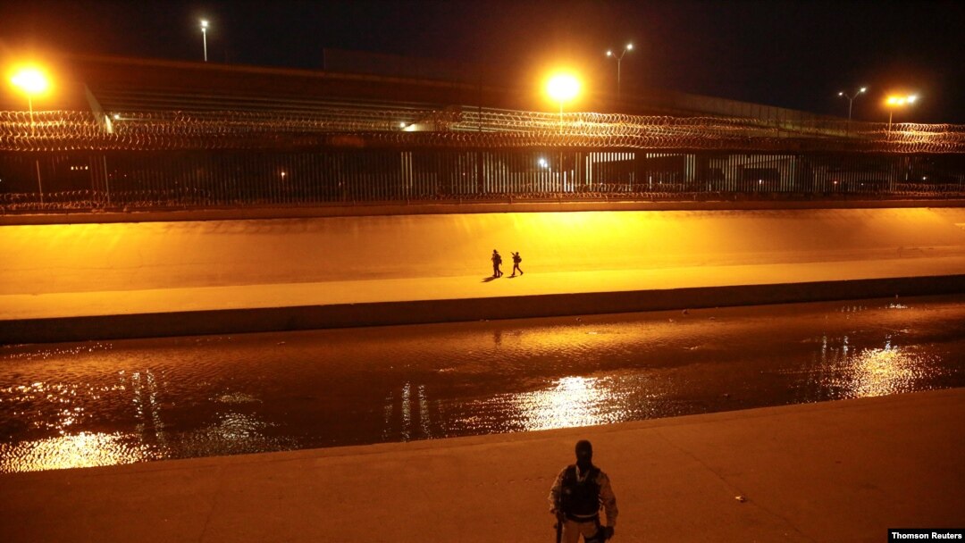 ARCHIVO - Migrantes en la orilla del Río Bravo luego de cruzarlo para entregarse a agentes de la Patrulla Fronteriza de EE. UU. para pedir asilo en El Paso, Texas, mientras un soldado de la Guardia Nacional Mexicana patrulla la frontera en Ciudad Juárez.