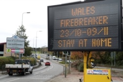 Traffic passes a COVID-19 sign informing drivers of the upcoming lockdown that closes nonfood retailers, cafes, restaurants, pubs and hotels for two weeks in a bid to reduce soaring coronavirus cases, in Cardiff, Wales, Oct. 23, 2020.