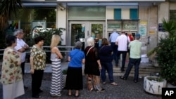 People stand in a queue to use an ATM outside a closed bank, next to a sign on the plant, bottom right, reading ''NO'' in Athens, June 30, 2015.