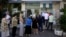 People stand in a queue to use an ATM outside a closed bank, next to a sign on the plant, bottom right, reading ''NO'' in Athens, June 30, 2015.
