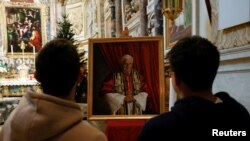 Para jemaat berkumpul di hadapan foto mantan Paus Benediktus di Gereja Santa Maria dell'Anima, di Roma, Italia 31 Desember 2022. (Foto: REUTERS/Ciro De Luca)