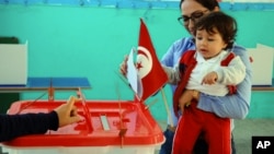 Une femme vote avec son enfant lors du premier tour de l'élection présidentielle tunisienne dans un bureau de vote à Marsa, près de Tunis, le 23 novembre 2014. 