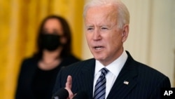 El presidente Joe Biden, en primer plano, se dirige a la nación desde la Casa Blanca, ante la atenta mirada de la vicepresidenta Kamala Harris, al fondo y con mascarilla, el 18 de marzo de 2021.