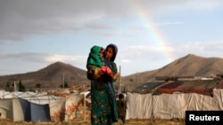 FILE - An internally displaced Afghan girl carries a child near their shelter at a refugee camp on the outskirts of Kabul, Afghanistan June 20, 2019. 