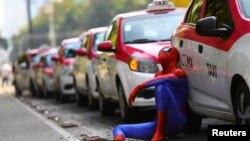 A person dressed up as Spider-Man sits next to a cab as taxi drivers hold a protest against taxi-hailing apps such as Uber, Cabify and Didi at Angel de la Independencia monument, in Mexico City, Oct. 12, 2020.