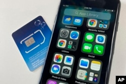 FILE - A SIM card is shown next to a cellphone in this photo taken on Tuesday, June 11, 2024 in London. Physical SIM cards are going away, replaced by eSIMs which make switching cell carriers easier. AP Photo/Kelvin Chan)