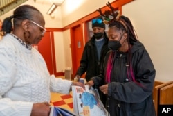 Tonya Williams, right, gets more papers to sell from Street Sense staff member Aida Peery, left, Wednesday, Dec. 6, 2023, in Washington. (AP Photo/Jacquelyn Martin)