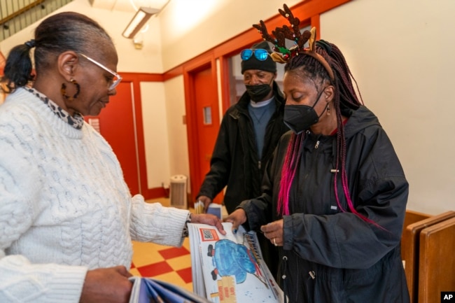 Tonya Williams, right, gets more papers to sell from Street Sense staff member Aida Peery, left, Wednesday, Dec. 6, 2023, in Washington. (AP Photo/Jacquelyn Martin)