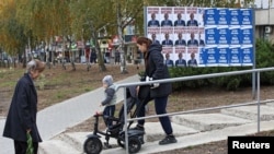 People walk past campaign posters of Moldova's incumbent President and presidential candidate Maia Sandu and presidential candidate Alexandr Stoianoglo in Chisinau, Moldova, Oct. 30, 2024. 