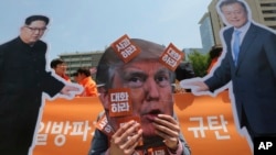 A protester wearing a mask of U.S. President Donald Trump, center, performs with cut-out photos of North Korean leader Kim Jong Un and South Korean President Moon Jae-in, right, during a rally against the United States' policies against North Korea near the U.S. embassy in Seoul, South Korea, May 25, 2018. The signs read "Apology." 