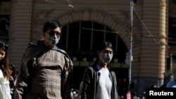 FILE - People wearing face masks walk by Flinders Street Station after cases of the coronavirus were confirmed in Melbourne, Australia, Jan. 29, 2020. 