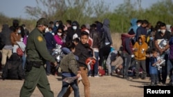 A U.S. Border Patrol Agent escorts two asylum-seeking unaccompanied minors from Central America as others take refuge near a baseball field after crossing the Rio Grande river into the United States from Mexico on rafts, in La Joya, Texas, March 19, 2021.