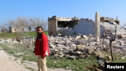 FILE - A man stands next to collapsed buildings after what activists said was an airstrike from forces loyal to Syria's president Bashar Al-Assad in Habeet, northern Idlib province, Dec. 26, 2014. 