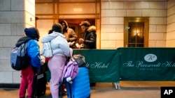 Sejumlah migrants menunjukkan surat-surat yang mereka miliki ke petugas keamanan di Hotel Roosevelt, di New York, pada 9 Januari 2024. (Foto: AP/Mary Altaffer)