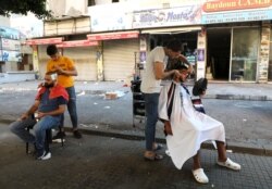 FILE - Barbers shave their customers outside their shop because of a power cut in Beirut, Lebanon, Aug. 20, 2021.