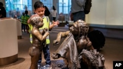 FILE - A boy pats the head of a sculpture of a Neanderthal boy, inside the Smithsonian Hall of Human Origins, Thursday, July 20, 2023, at the Smithsonian Museum of Natural History in Washington.