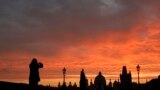 Woman takes a photograph of the medieval Charles Bridge as the sun rises in Prague, Czech Republic.