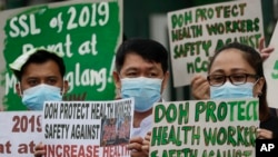 FILE - Health workers wearing protective masks hold signs during a rally outside a hospital in metropolitan Manila, Philippines, Feb. 7, 2020, demanding the government ensure their safety and raise their pay amid to the coronavirus threat.