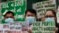 FILE - Health workers wearing protective masks hold signs during a rally outside a hospital in metropolitan Manila, Philippines, Feb. 7, 2020, demanding the government ensure their safety and raise their pay amid to the coronavirus threat.