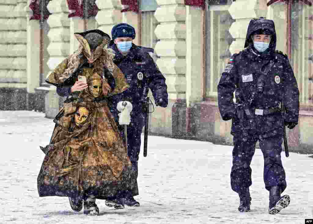 Two police officers and a woman in a carnival costume walk in the snowfall, in Moscow, Russia.