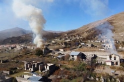 Smoke rises from burning houses as people leave the separatist region of Nagorno-Karabakh for Armenia, Nov. 14, 2020. The territory is to be turned over to Azerbaijan Nov. 15.