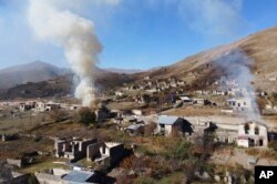 Smoke rises from burning houses as people leave the separatist region of Nagorno-Karabakh for Armenia, Nov. 14, 2020. The territory is to be turned over to Azerbaijan Nov. 15.