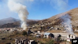 In this photo taken with a drone, smoke rises from burning houses as people leave the separatist region of Nagorno-Karabakh for Armenia, Nov. 14, 2020. The territory is to be turned over to Azerbaijan Nov. 15. 