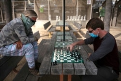 FILE - Wearing face coverings, John Williams, right, and Jeff Lee play chess, June 23, 2020, in Santa Monica, Calif.