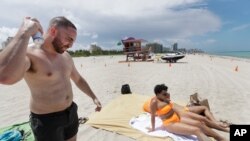 Cameron Baca, left, of Riverside County, California, puts on sunscreen while at Miami Beach, Florida's famed South Beach, July 7, 2020. 