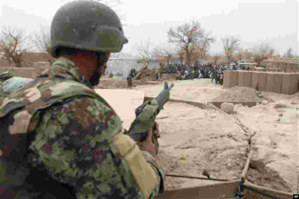 An Afghan soldier is seen in a guard tower at a military base as civilians gather outside in Panjwai, Kandahar province south of Kabul, Afghanistan, Sunday, March 11, 2012. Afghan President Hamid Karzai says a U.S. service member has killed more than a do