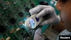 FILE - A woman looks through a magnifying glass to check for errors on a printer circuit board at Manutronics Factory in Bac Ninh province, Vietnam, May 30, 2018. 