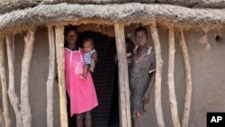 In this photo taken May 2, 2018, children stand in the doorway of their home as they watch their mother prepare food she received from an aerial food drop by the World Food Program in the town of Kandak, South Sudan. 