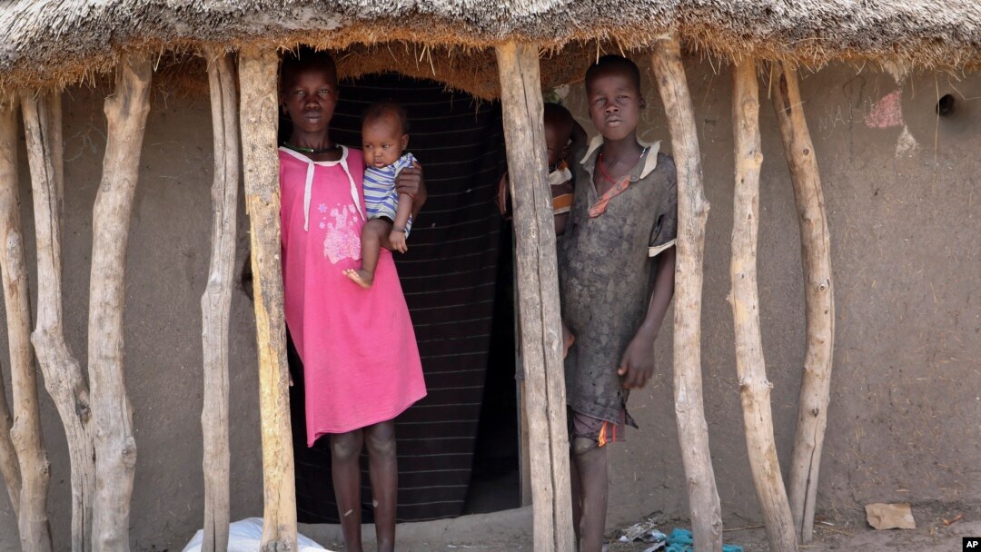 Children stand in the doorway of their home as they watch their mother prepare food she received from an aerial food drop by the World Food Program in the town of Kandak, South Sudan, May 2, 2018. 