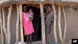 Children stand in the doorway of their home as they watch their mother prepare food she received from an aerial food drop by the World Food Program in the town of Kandak, South Sudan, May 2, 2018. 