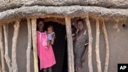 FILE - In this May 2, 2018, photo children stand in the doorway of their home as they watch their mother prepare food she received from an aerial food drop by the World Food Program in the town of Kandak, South Sudan. 