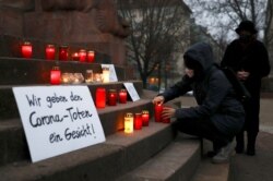 A person wearing protective mask lights a candle on a vigil organised by activist-group #wirgebendenToteneinGesicht (We give a face to the dead) to commemorate the people who died due to COVID-19 in Berlin, Germany, Dec. 13, 2020.