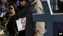 FILE - A man carries a portrait of slain journalist Hector Gonzalez Antonio as his daughter, left, mourns during his funeral in Mexico City, Mexico, May 31, 2018.