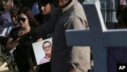 FILE - A man carries a portrait of slain journalist Hector Gonzalez Antonio as his daughter, left, mourns during his funeral in Mexico City, Mexico, May 31, 2018.