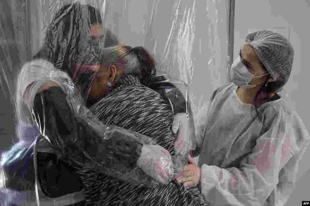 Suzane Valverde (L) hugs her 85-year-old mother Carmelita Valverde, through a transparent plastic curtain at a senior nursing home in Sao Paulo, Brazil, June 13, 2020, amid the novel coronavirus (COVID-19) pandemic.