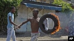 A supporter of Ivory Coast opposition leader Alassane Ouattara carry a burning tire during a protest in the city of Abidjan, Ivory Coast, Saturday, Dec. 4, 2010.