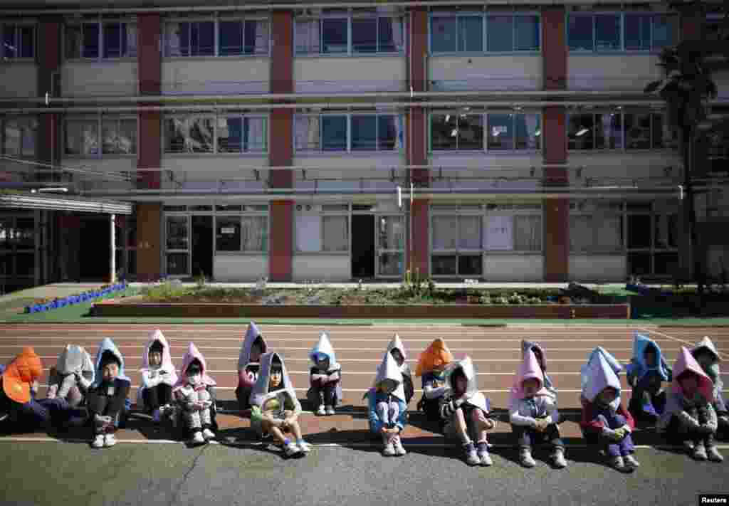 School children wearing padded hoods to protect them from falling debris sit on running track during an earthquake simulation exercise at an elementary school in Tokyo, Japan.