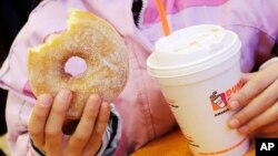 FILE - A girl has a doughnut and a beverage in New York, Feb. 14, 2013. A new study finds more than half the calories consumed in the average American diet comes from "ultra-processed" foods, including sugary drinks.