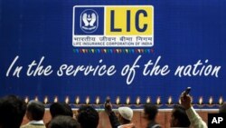 Indian bystanders watch an art performance in front of a billboard for the Life Insurance Corporation of India (LIC) outside the company's offices in New Delhi, India, Nov. 25, 2010. Eight senior officials from some of India's top financial services comp