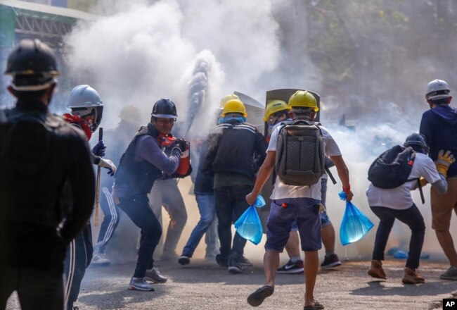 FILE - Anti-coup protesters use fire extinguishers to reduce the impact of teargas fired by riot policemen in Yangon, Myanmar, March 9, 2021.