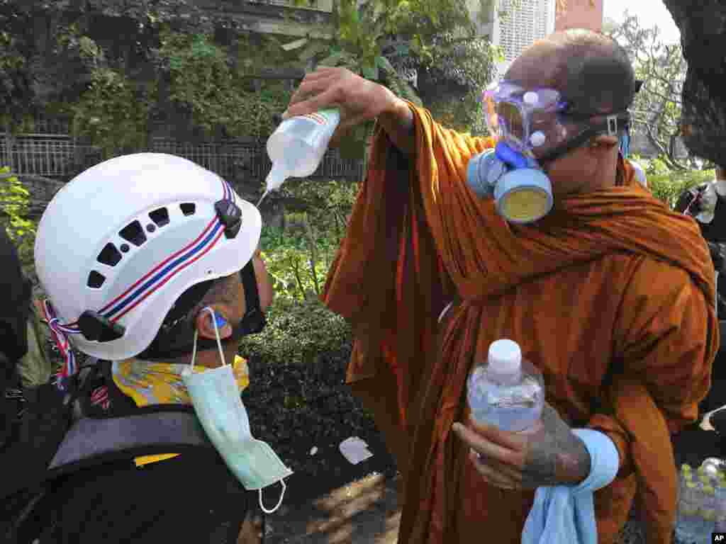 A Buddhist monk helps an anti-government protester clean his eyes with salt water solution after riot police fired tear gas in Bangkok, Dec. 2, 2013.