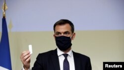 FILE - French Health Minister Olivier Veran, wearing a protective face mask, holds a COVID test during a news conference at Bichat hospital in Paris, France, Oct. 1, 2020. Veran's home was among those searched as part of a COVID response probe.